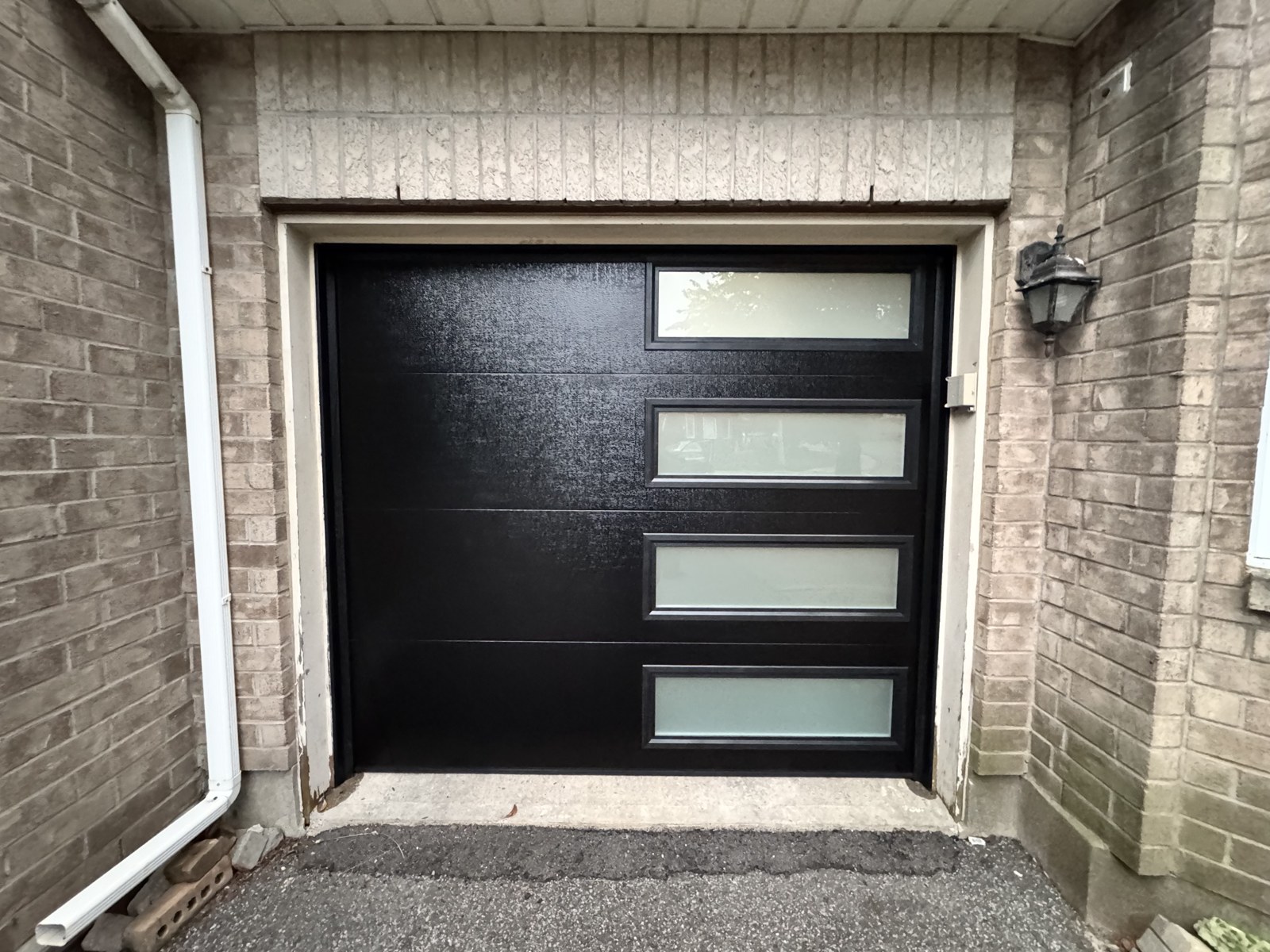 Single black modern garage door with frosted window inserts on a brick home in Ottawa