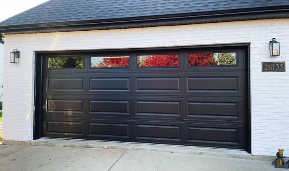 Black long-panel garage door with window inserts on a white brick home, garage door replacement Ottawa